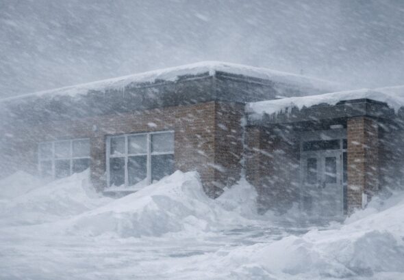 An empty school building exterior in Thompson, Manitoba during a severe blizzard with heavy blowing snow and dark overcast skies.